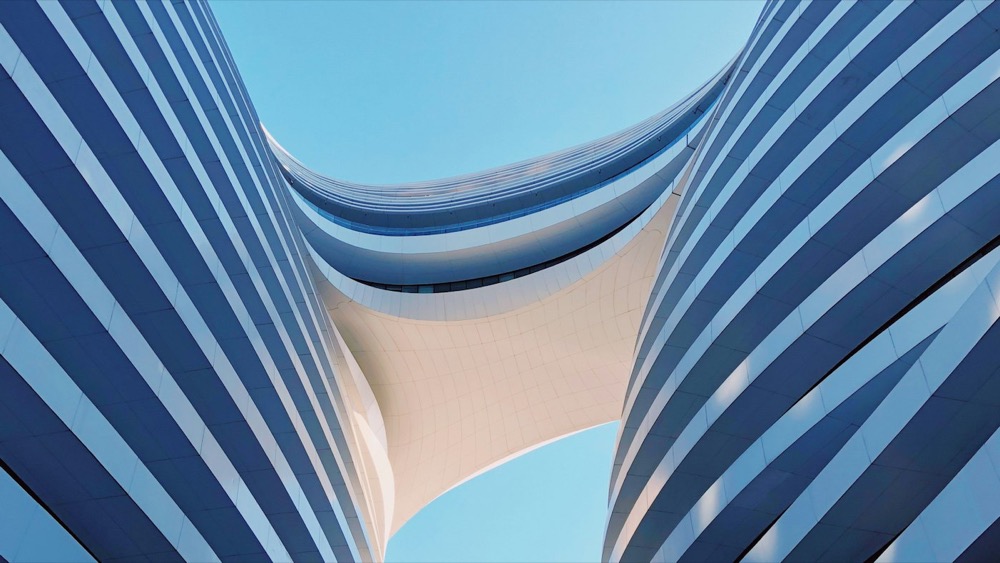 Curved concrete bays of a modern building seen from below, converging towards an open sky